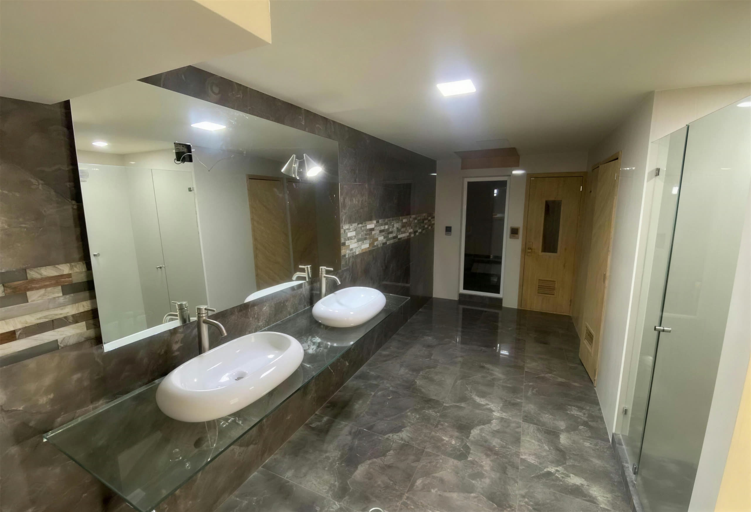 Baño del gimnasio con doble lavamanos y acceso al sauna
