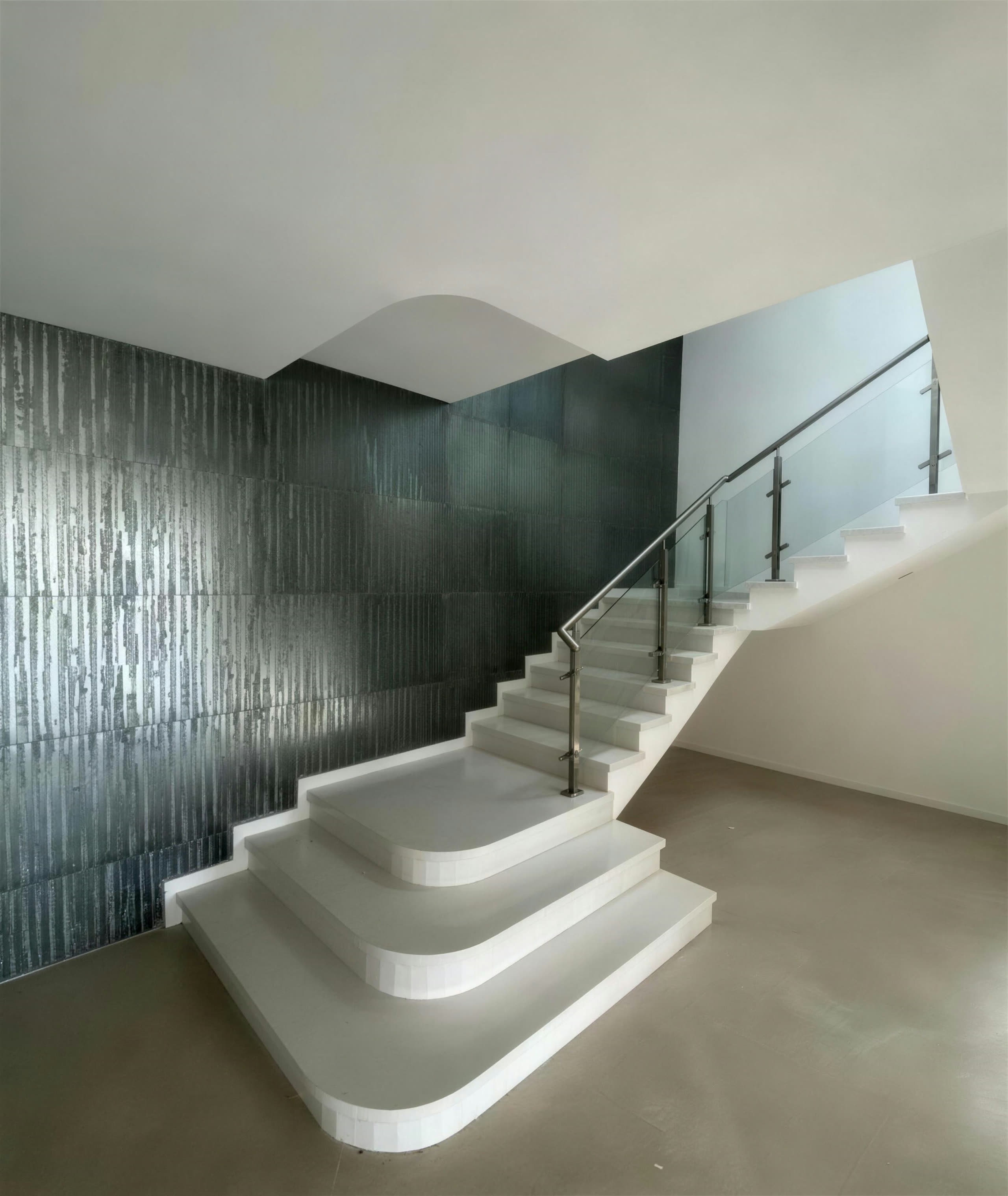 Escalera escultórica blanca con muro de acero envejecido