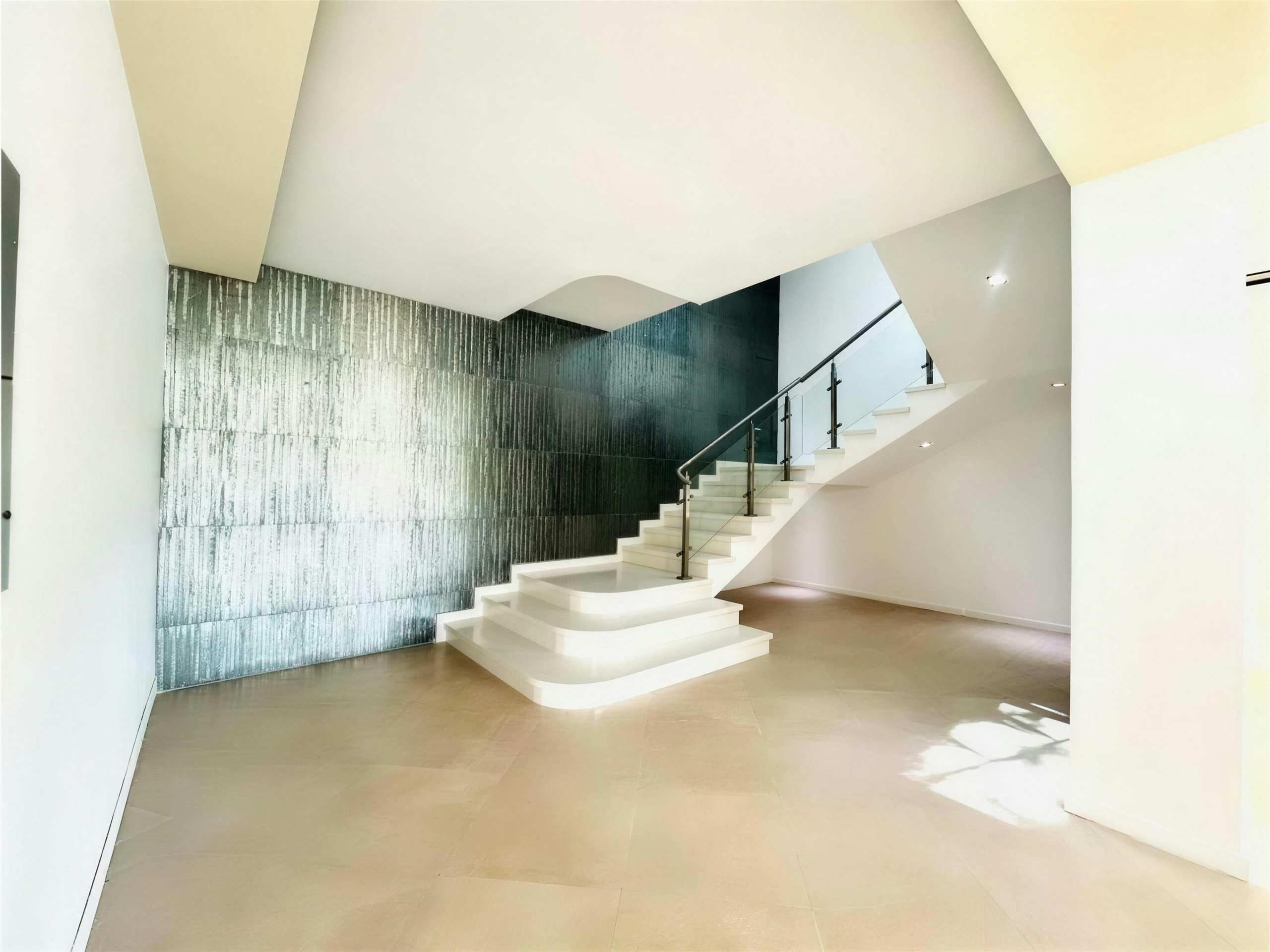 Escalera principal con muro texturizado y baranda de vidrio